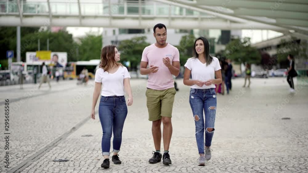 Cheerful people having pleasant conversation during stroll. Full length shot of smiling relaxed friends walking on street and talking. Communication concept Cheerful people having pleasant conversation during stroll. Full length shot of smiling relaxed friends walking on street and talking. Communication concept