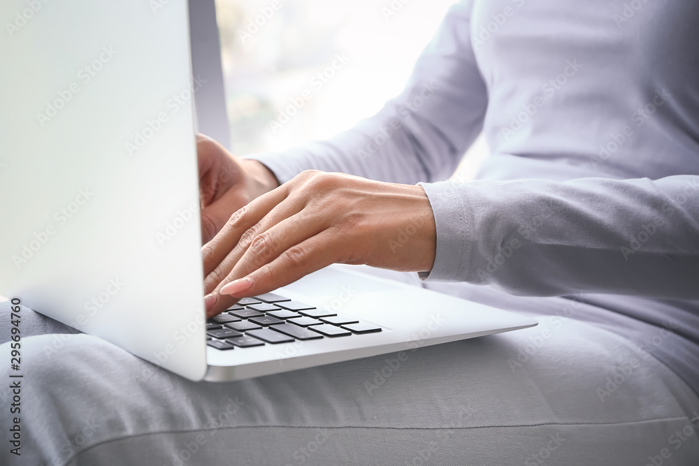 Young woman working on laptop near window, closeup Young woman working on laptop near window, closeup