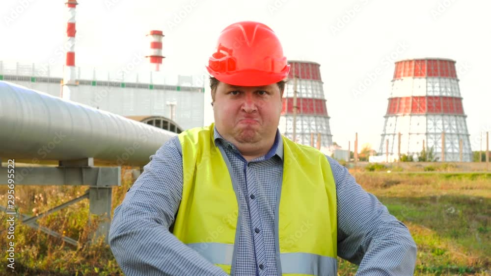 Worker, engineer, or electrician looking at the camera employee shows how to work standing in front of a power station Worker, engineer, or electrician looking at the camera employee shows how to work standing in front of a power station