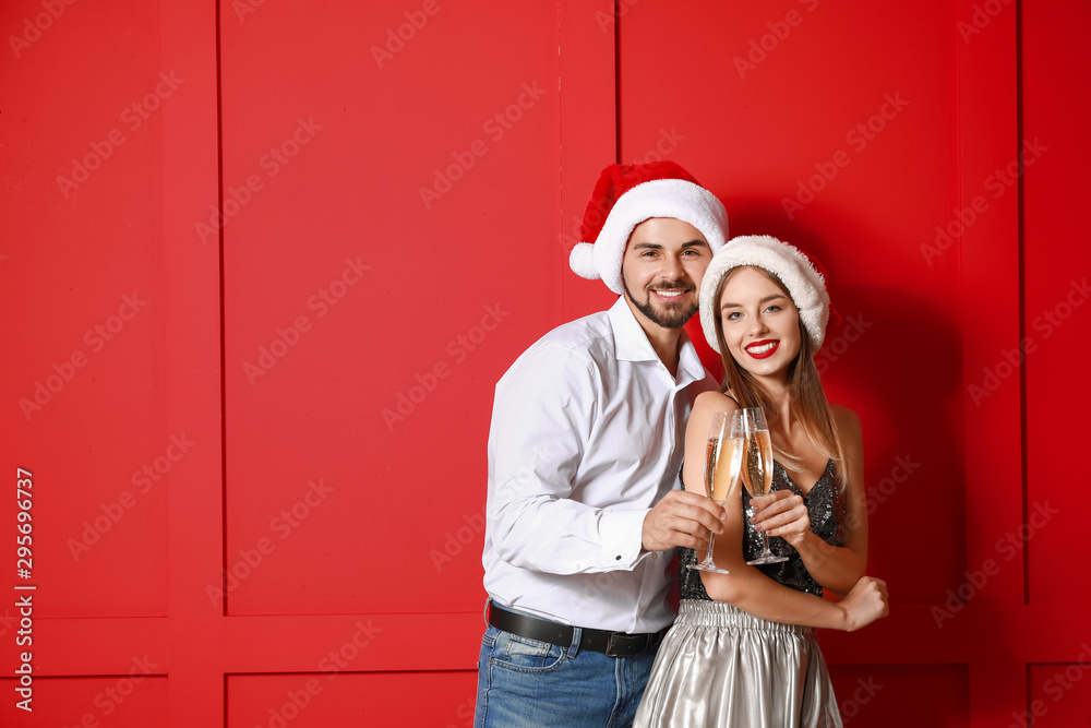 Fototapeta premium Happy young couple in Santa hats and with champagne on color background