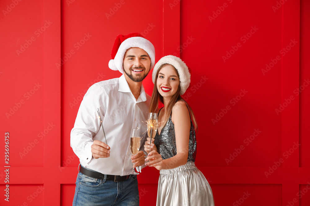 Fototapeta premium Happy young couple with Christmas sparklers and champagne on color background