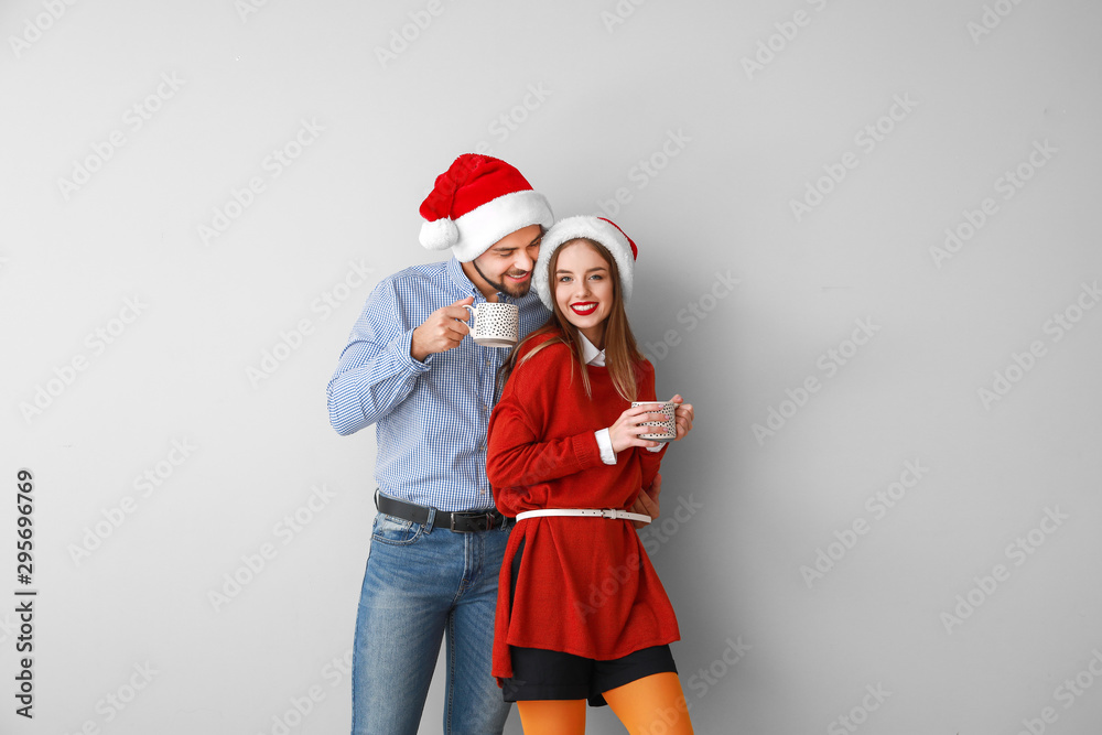 Obraz premium Happy young couple in Santa hats and with hot chocolate on light background