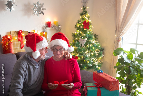 Let's celebrate Christmas together. A beautiful elderly couple enjoying the exchange of gifts. They wear Santa's hats. Beautiful Christmas tree in the background and gifts for the family