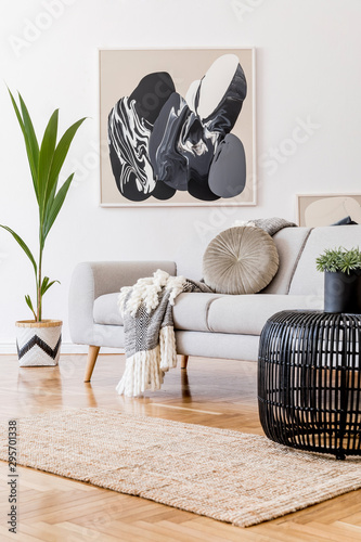 Stylish and design home interior of living room with gray sofa, rattan table, lamp, tropical leaf, plaid, pillows and elegant decoration. Abstract mock up paintings frame on white walls. Template.