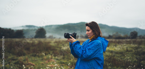 photographer tourist girl in blue raincoat hold in hands photo camera take photography foggy mountain, traveler shooting nature, click on camera technology, landscape vacation concept free space
