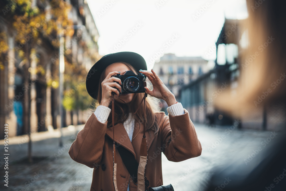 Outdoor smiling lifestyle portrait of pretty young woman having fun in sun city Europe autumn with camera travel photo of photographer Making pictures in glasses and hat with girlfriends - obrazy, fototapety, plakaty 