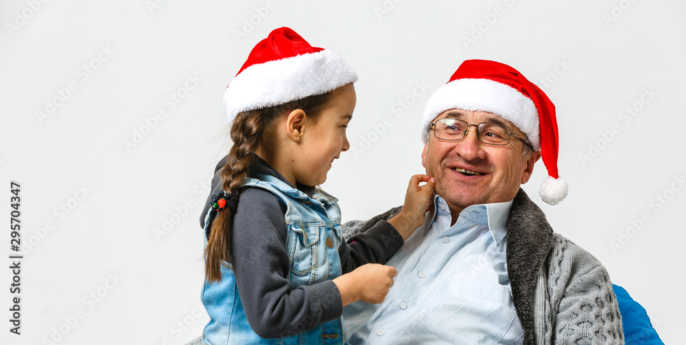 A small girl and senior grandfather with Santa hat hugging at Christmas time. A small girl and senior grandfather with Santa hat hugging at Christmas time.