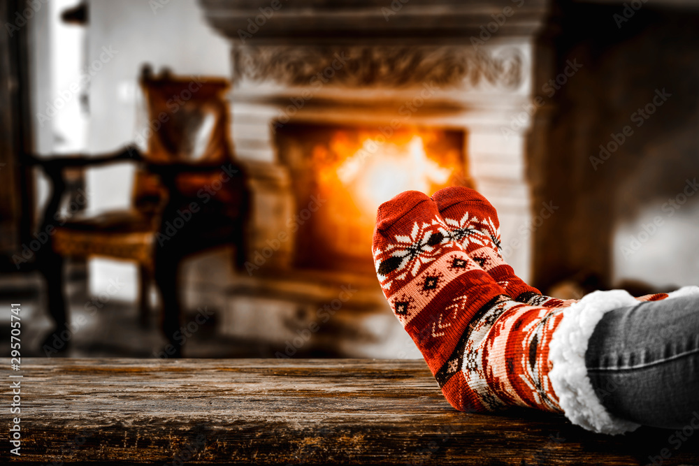 Christmas socks with woman legs on wooden board of free space for your decoration and blurred background of fireplace  - obrazy, fototapety, plakaty 