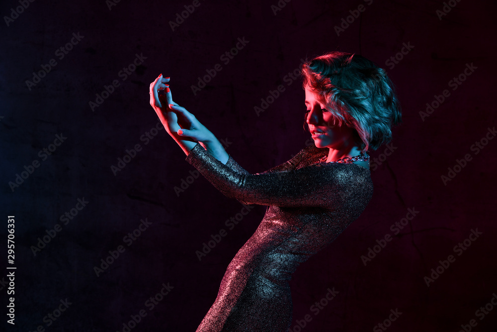 Attractive young girl in a tight shiny dress in the studio with color filters. - obrazy, fototapety, plakaty 