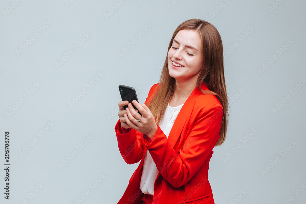 Naklejka premium girl in a red jacket is typing a message on the phone on a gray light background