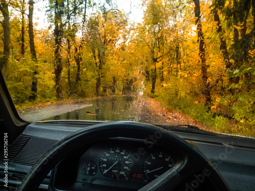 Road in the autumn forest in rain. Asphalt road in overcast rainy day. Roadway with reflection and trees in kaliningrad region. Empty highway in fall woodland. Rain drops on the windshield of a car.