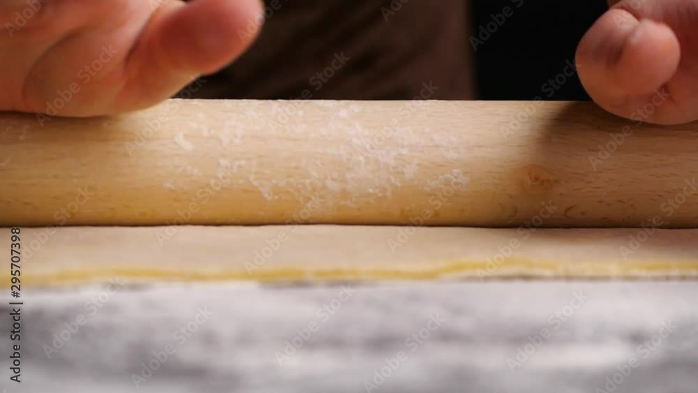 Female hands rolling dough with rolling pin for pastry on black wooden table. Slowmotion. Female hands rolling dough with rolling pin for pastry on black wooden table. Slowmotion.