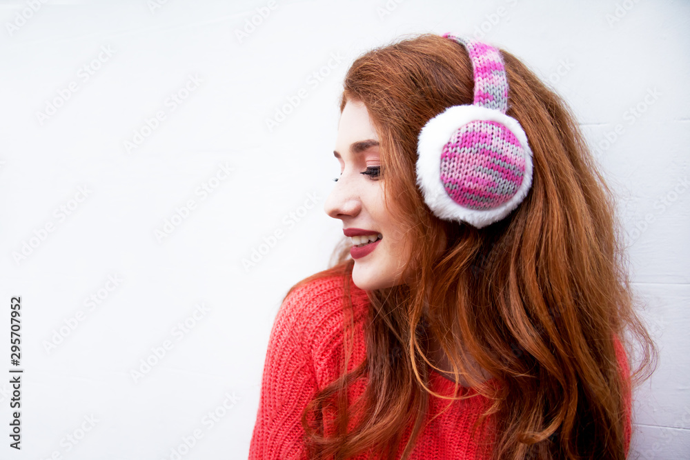 Naklejka premium Young beautiful woman posing against the white wall. Girl wearing warm orange sweater and headphone.