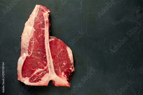 Raw t-bone steak with fresh herbs on a concrete or slate background, top view, place for text,