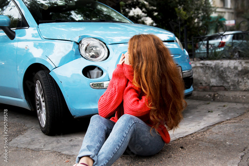 Upset woman sit on a road and cry after damage her new car.broken car parked on road.