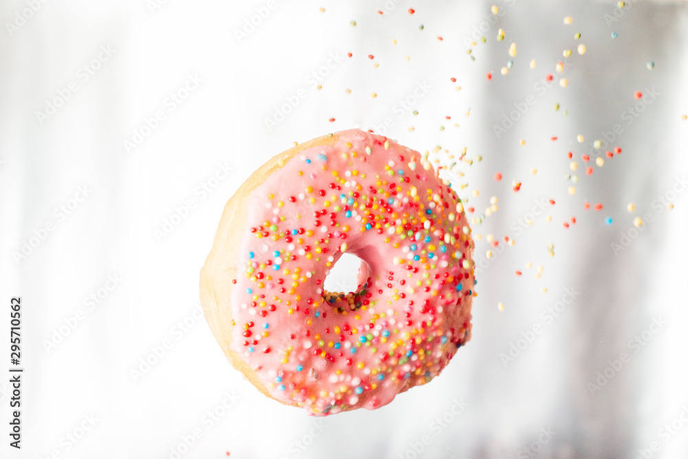 Pink donut with pastry topping and flying rainbow colored Sprinkles
