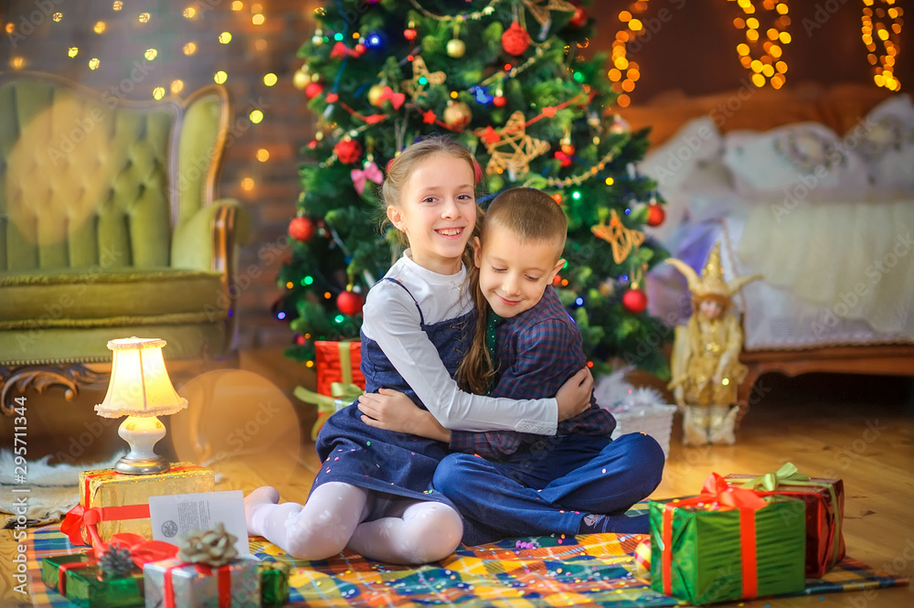 Christmas time, cute children play cuddling and having fun sitting on the floor near the festive Christmas tree