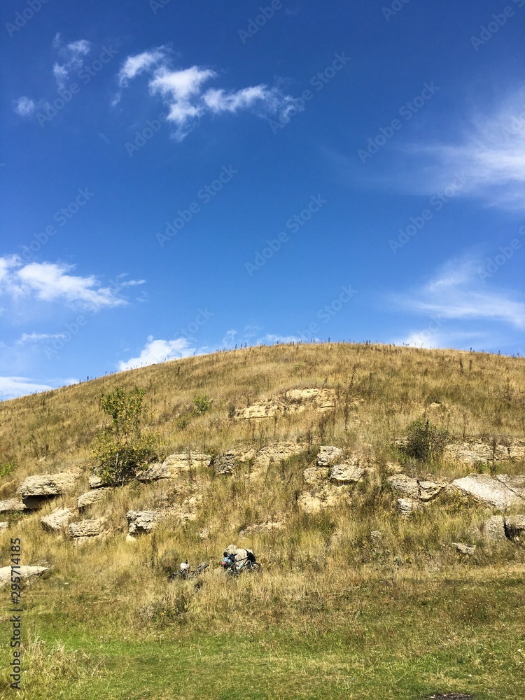 Hiking concept. High hill with rocks and bicycles at foot against clear blue sky Hiking concept. High hill with rocks and bicycles at foot against clear blue sky