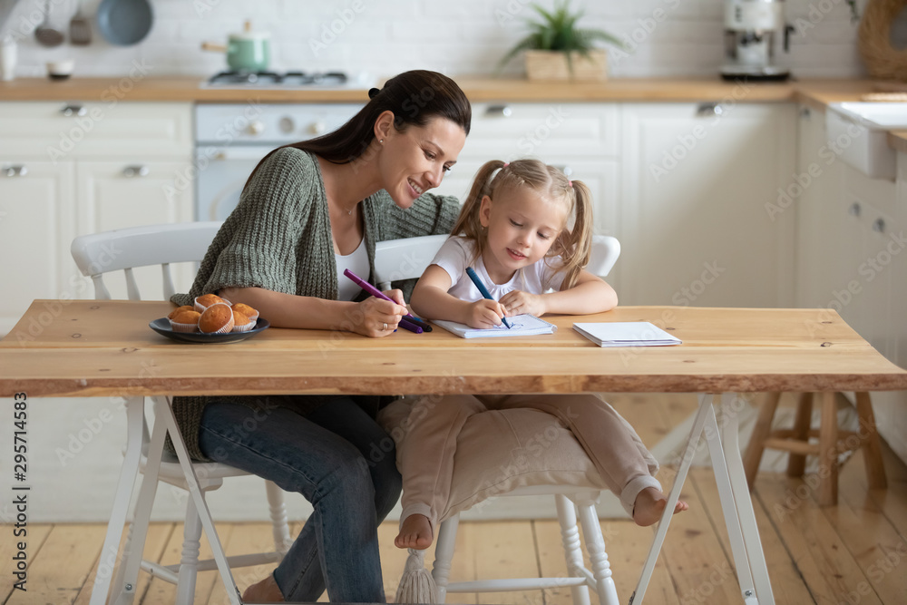 Smiling mother and little daughter drawing felt-tip pens in kitchen Smiling mother and little daughter drawing felt-tip pens in kitchen