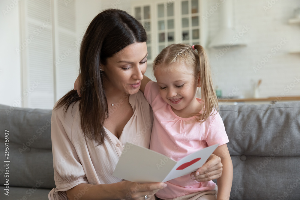 Happy mother embracing little daughter, reading greeting card Happy mother embracing little daughter, reading greeting card