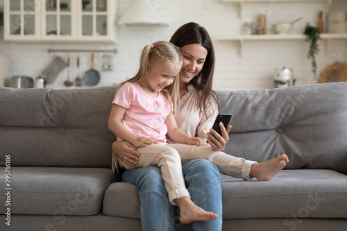 Happy young mother and little daughter having fun with phone