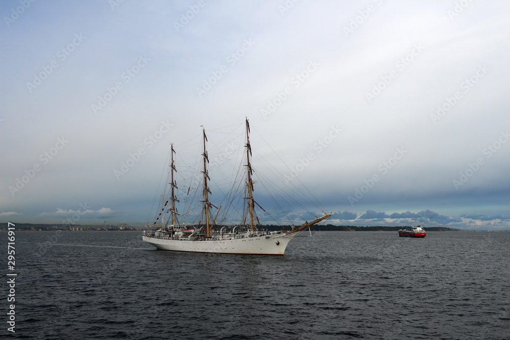 Obraz premium Training sailing frigate goes to sea from the port against a stormy sky