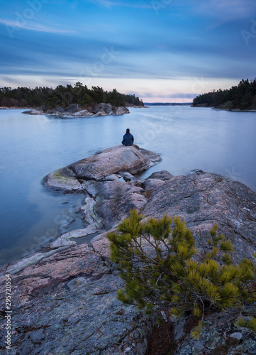 Canvas Print A lone man sits by the edge of the ocean as the sun sets