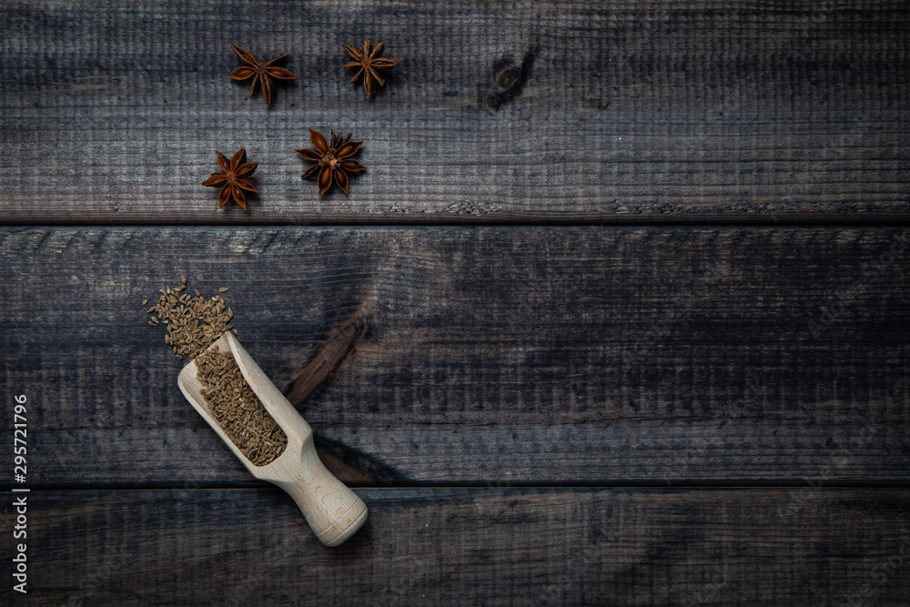Fototapeta premium Anise stars and scoop of anise on a dark wooden table. The concept of using spices for dishes, enriching the taste.