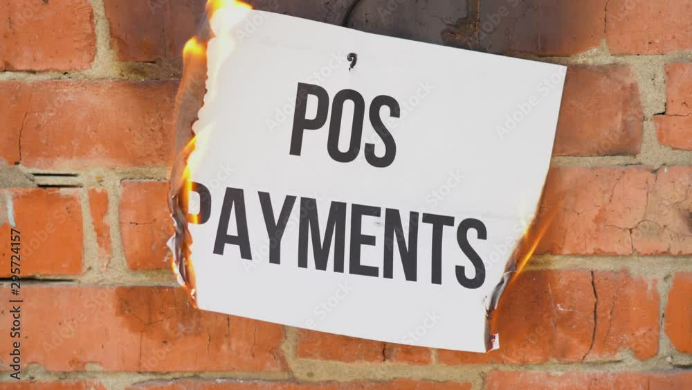 The inscription on a white A4 size sheet against the background of an orange brick wall. The paper with the black word Pos Payments burns, smoke and turns into ashes. Business concept. The inscription on a white A4 size sheet against the background of an orange brick wall. The paper with the black word Pos Payments burns, smoke and turns into ashes. Business concept.