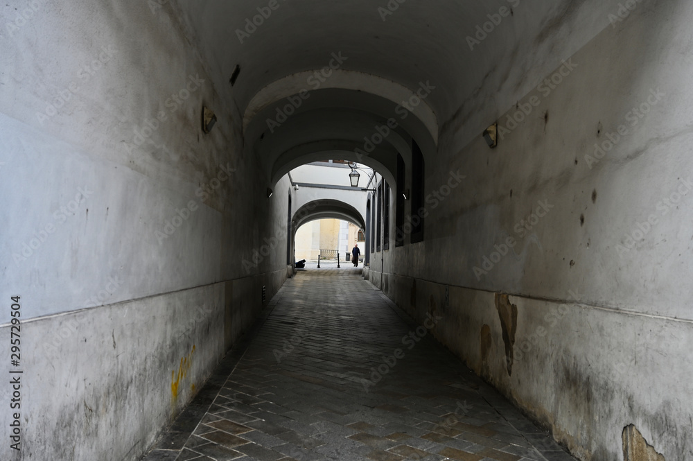 Stone Arched Tunnel Through Buildings with Paved Walkway and Figure at Far End