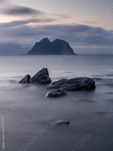 Misty waves cover coastal rocks with a remote rocky island in the background