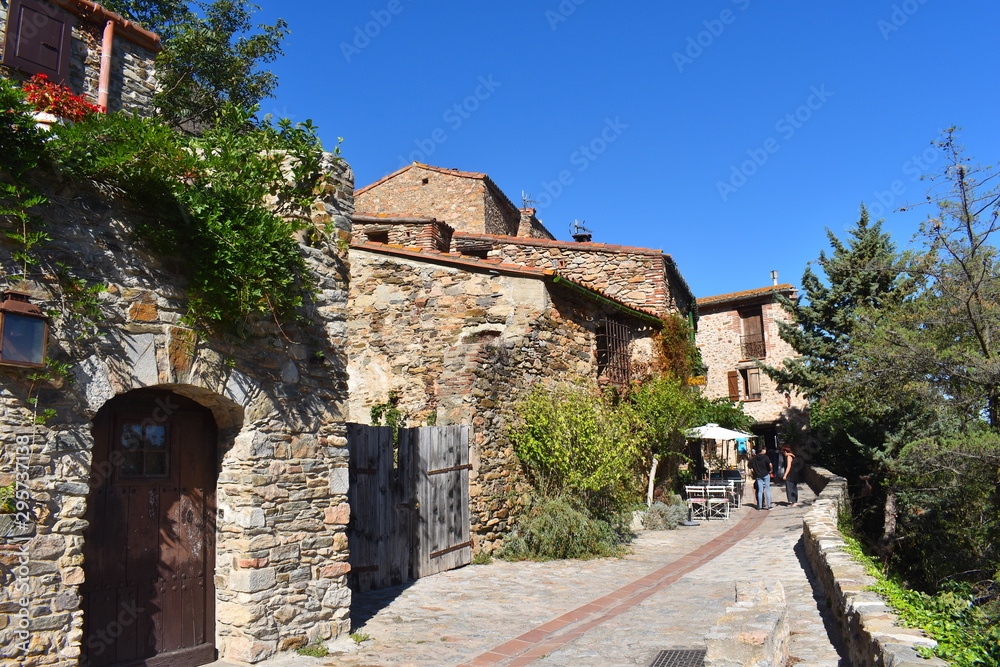 Charming cobblestone pedestrian only street in a medieval European town. Stone two storey houses dotted with wooden shutters, gates and exotic greenery on a sunny day.