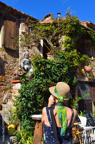 Back of a woman with straw hat and summer dress taking photos of a stone wall with greenery. Bright sunny day in a medieval European old town.  photo