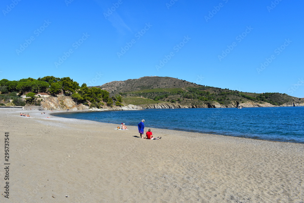 Beach goers enjoying a bright sunny clear blue sky day on a miles long sandy beach on the French Riviera. Cliffs and vineyards at the background. 