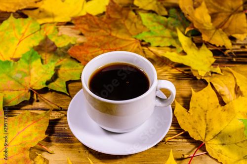 Cup of coffee and heap of yellow maple leaves on a wooden table