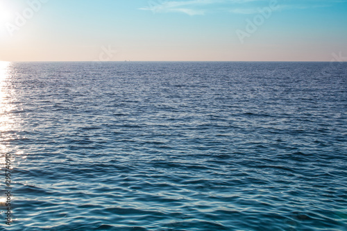 Horizon on the sea. Sun reflects in the water in the small waves. A pair of white clouds are hanging over the water.