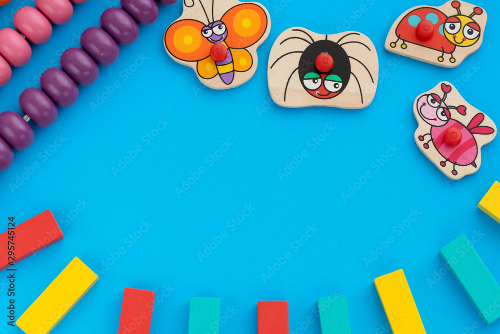 Frame from kids toys, top view on children's educational games on blue paper background. Multicolored wooden bricks, abacus, cute butterfly, ladybug, bee, spider. Flat lay, copy space for text Frame from kids toys, top view on children's educational games on blue paper background. Multicolored wooden bricks, abacus, cute butterfly, ladybug, bee, spider. Flat lay, copy space for text