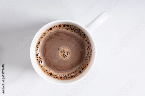 White ceramic cup of hot cocoa on top of white marble background, top view