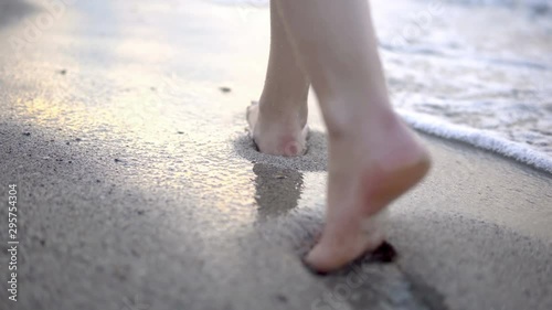 Beach travel - woman walking on sand beach leaving footprints in the sand. Closeup detail of female feet and golden sand photo