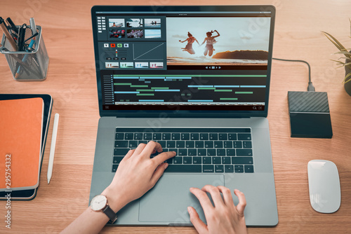 Billede på lærred Concept of simple operation of blogger and vlogger, hand using laptop on video editor works with footage on wooden table, camera and accessories on table