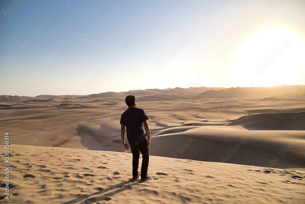 young man on sand in a desert near Huacachina, Ica region, Peru. The sunset desert view