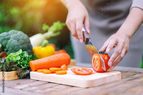 Canvas Print Closeup image of a woman cutting and chopping tomato by knife on wooden board