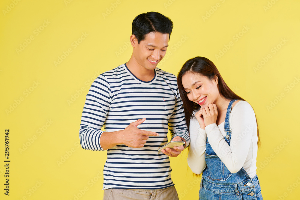 Smiling handsome young Asian man reading text message with exiting news to girlfriend Smiling handsome young Asian man reading text message with exiting news to girlfriend