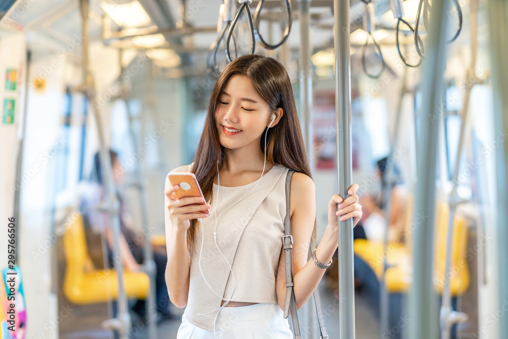 Young Asian woman passenger listening music via smart mobile phone in subway train when traveling in big city,japanese,chinese,Korean lifestyle and daily life, commuter and transportation concept