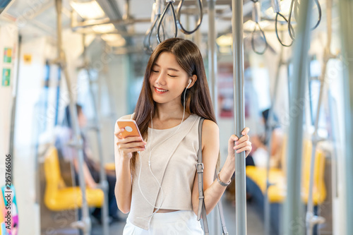 Obraz na płótnie Young Asian woman passenger listening music via smart mobile phone in subway train when traveling in big city,japanese,chinese,Korean lifestyle and daily life, commuter and transportation concept w salonie