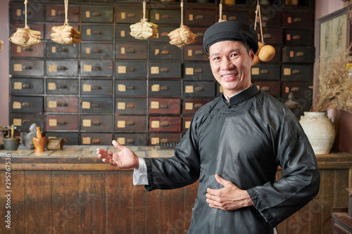 Obraz na plátně Happy Asian man making welcoming gesture and inviting customers to traditional C