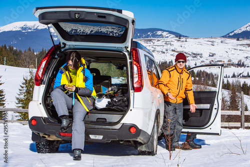 woman with man near suv car opened trunk full of ski and snowboarding stuff changing boots