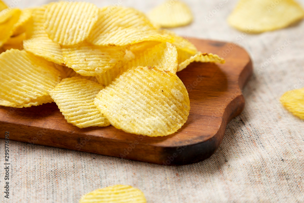Salted wavy potato chips on a rustic wooden board, side view. Close-up.