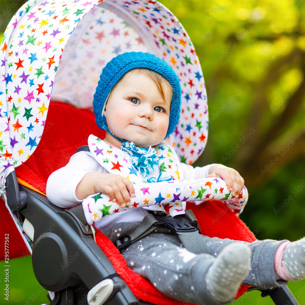 Cute Healthy Little Beautiful Baby Girl With Blue Warm Hat Sitting In The Pram Or Stroller