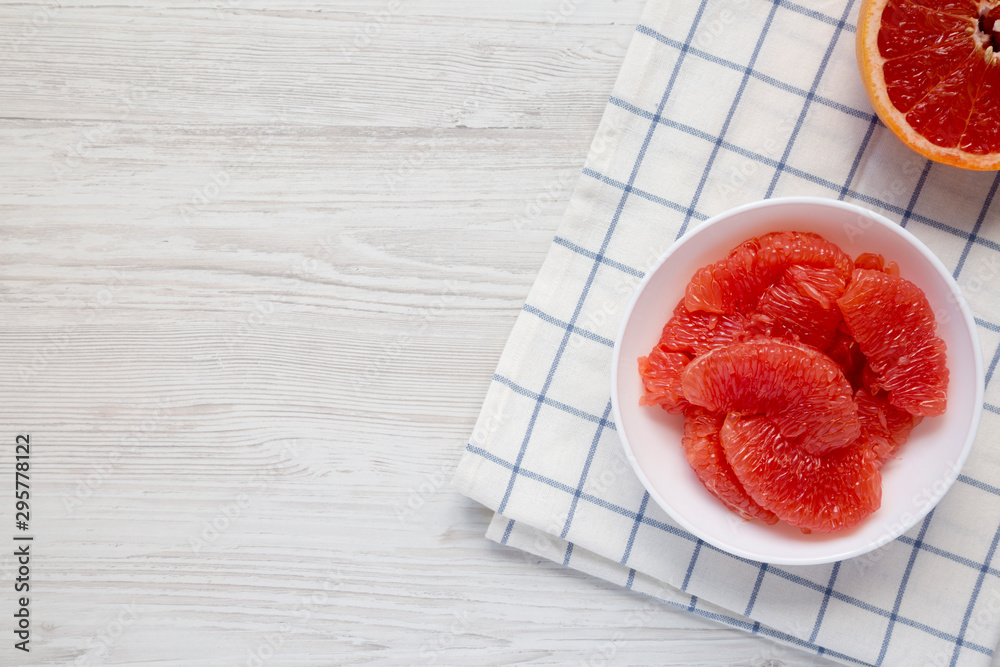 Red grapefruit slices in a white bowl on a white wooden surface, top view. Flat lay, overhead, from above. Copy space. Red grapefruit slices in a white bowl on a white wooden surface, top view. Flat lay, overhead, from above. Copy space.